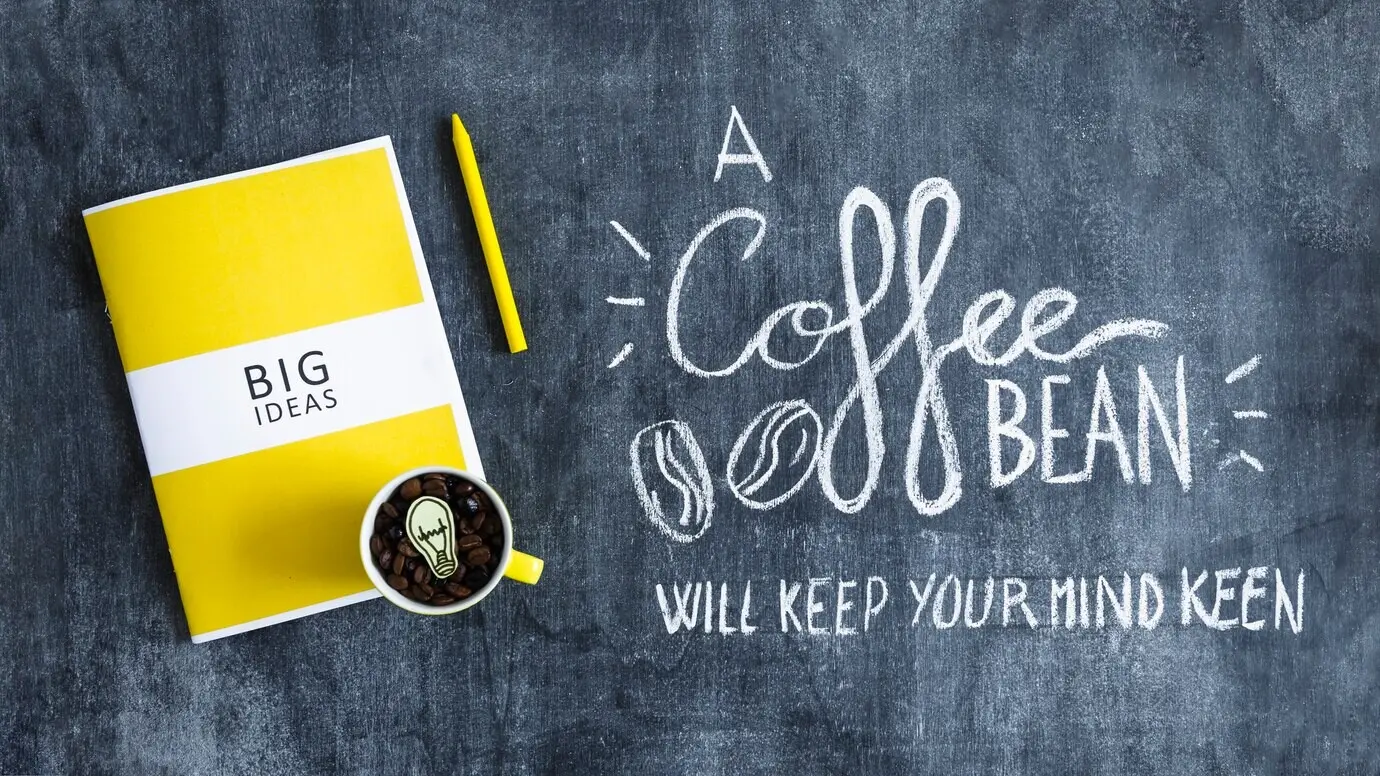 Becher mit Kaffeebohnen, mit einer Glühbirne über dem Buch „Big Ideas“ und Text auf einer Tafel.